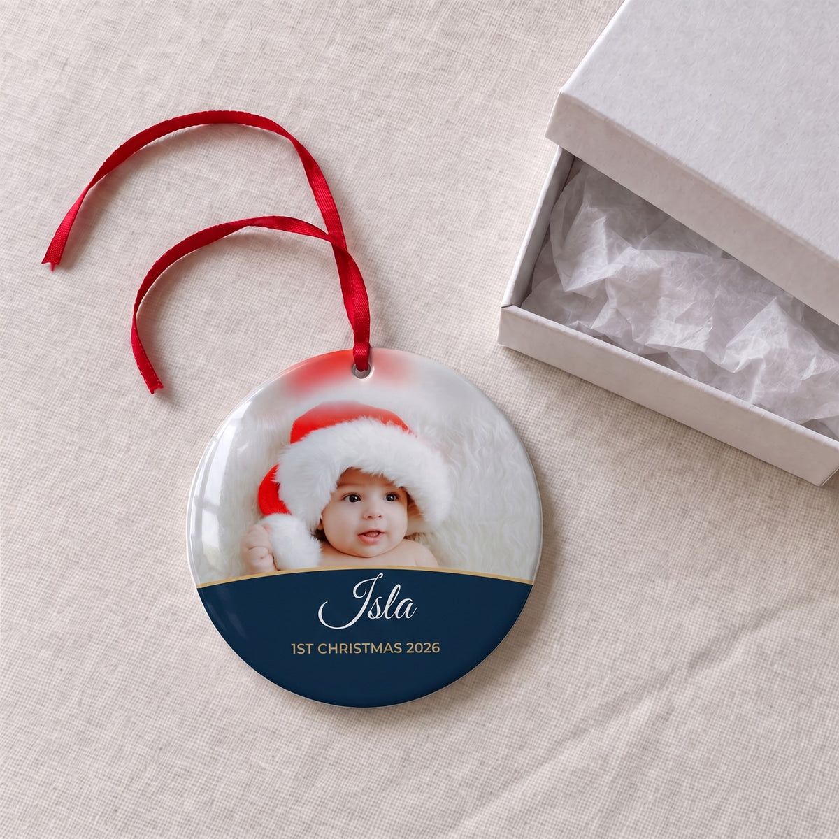 Midnight blue personalised Baby's 1st Christmas photo bauble on a tablecloth beside a white gift box