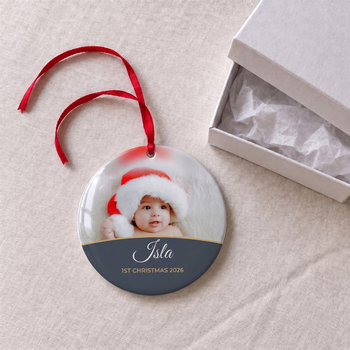 Slate personalised Baby's 1st Christmas photo bauble on a tablecloth beside a white gift box