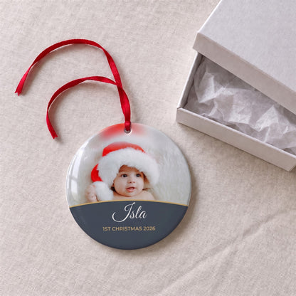 Slate personalised Baby's 1st Christmas photo bauble on a tablecloth beside a white gift box